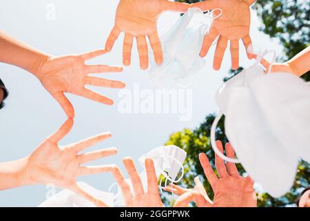 Foto-Unterseite der Menschen Handflächen, die sich mit den kleinen Fingern und Daumen halten, während sie medizinische Masken in die Luft werfen. Stockfoto