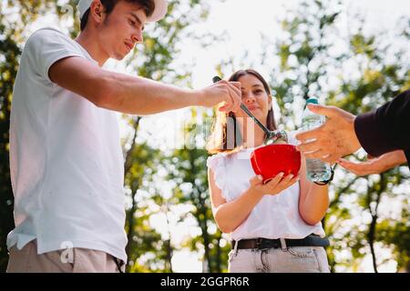 Ein paar Freiwillige, die einem Obdachlosen helfen, geben ihm eine Schüssel Suppe und eine Plastikflasche Wasser, Freiwilligenmission Konzept. Stockfoto