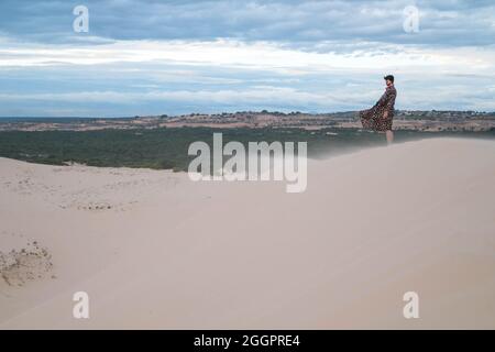 Wanderer beim Wandern in der Wüste. Junger Mann, der in weißen Sanddünen steht. Fremder in der Wüste. Sand fliegt im Wind. Kleidung flattert im Wind Stockfoto