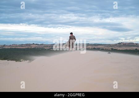 Wanderer beim Wandern in der Wüste. Junger Mann, der in weißen Sanddünen steht. Rückansicht. Fremder in der Wüste. Sand fliegt im Wind Stockfoto