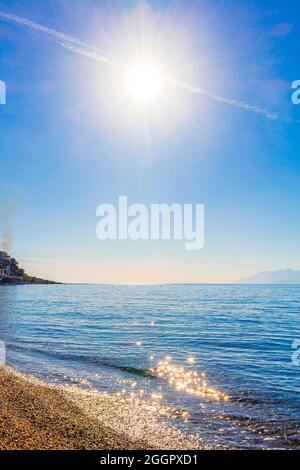 Chemtrail überqueren Sie die Sonne über dem blauen Himmel und den Strand auf der Insel Kos in Griechenland. Stockfoto