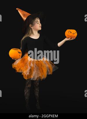 Ein lustiges Mädchen mit langen Haaren mit zwei Jack Kürbissen und in einem Hexenkostüm für Halloween Feier. Orangefarbener Hut und Rock, schwarze Bluse, Spinnennetz Stockfoto