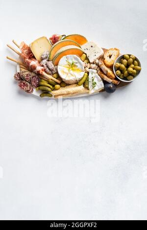 Verschiedene Käsesorten auf Holzbrettteller, Oliven, Trauben, Brot auf weißem Hintergrund, Draufsicht, flach liegend, Kopierraum. Stockfoto