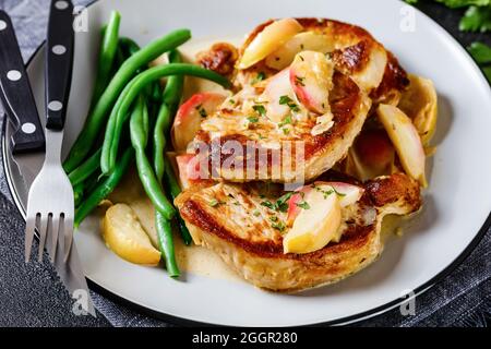 Apfelmost Glasierte Schweinekoteletts mit grünen Bohnen und karamellisierten Apfelscheiben auf einem Teller mit Besteck Stockfoto