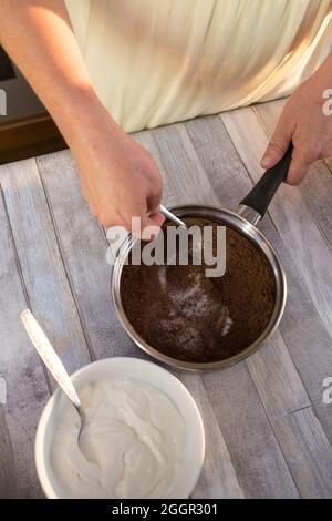 Der Prozess der Herstellung von Schokolade Glasur. Schritt für Schritt. Die Zutaten werden in einem Topf gemischt. Langsam aufwärmen, um sich aufzulösen. Stockfoto