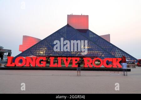 Dämmerungsansicht der Rock and Roll Hall of Fame, entworfen vom Architekten I.M.Pei. Mit Long Live Rock-Schild im Vordergrund.Cleveland.Ohio.USA Stockfoto