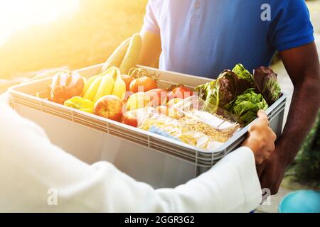 African Man Lebensmittelgeschäft Lieferung. Frau Nimmt Gemüsekratte Stockfoto
