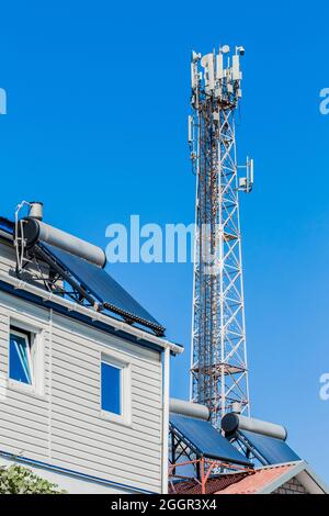 Sonnenkollektoren und Warmwasserbereiter alternative Energie auf den Dächern von Häusern vor dem Hintergrund einer mobilen Zelle Turm Kommunikation. Stockfoto