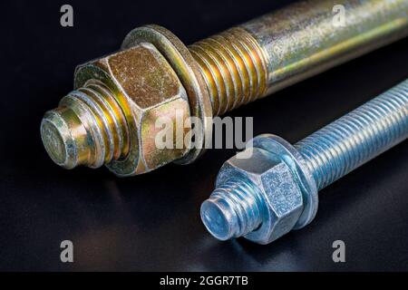 Metallmuttern und -Unterlegscheiben auf verzinkten Schrauben mit Reflektion auf schwarzem Hintergrund. Enden von zwei Keildehnungsankern zur Befestigung in Beton. Stockfoto