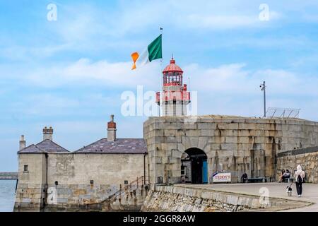 Der Leuchtturm am East Pier in Dun Laoghaire, Dublin, Irland mit der Flagge der Irischen Republik bei vollem Mast über dem Kopf. Leuchtturm erbaut 1847. Stockfoto