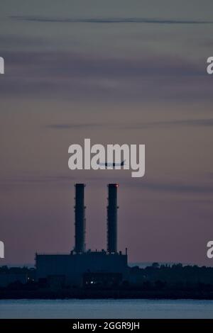 Blick am frühen Morgen auf das Flugzeug, das über das Pigeon House Power Station mit sichtbarer Wärmeverzerrung auf Rauch von Blackrock, Dublin, aus gesehen wird Stockfoto