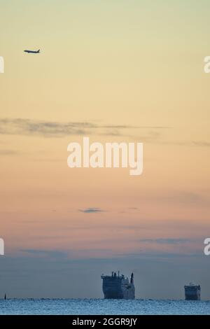 Wunderschöne Aussicht am frühen Morgen auf zwei See-LKW-Fährschiffe in der Irischen See und das Flugzeug über Howth von Blackrock Beach, Dublin, Irland. Weichfokus Stockfoto