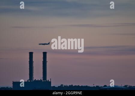 Blick am frühen Morgen auf das Flugzeug, das über das Pigeon House Power Station mit sichtbarer Wärmeverzerrung auf Rauch von Blackrock, Dublin, aus gesehen wird Stockfoto