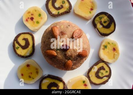 Indische Süßigkeiten Weizen oder Atta laddu, Schokolade Barfi, tutti fruchtigen Burfi auf weißem Hintergrund angeordnet. Süße Dessertartikel, die während fe sortiert und serviert werden Stockfoto