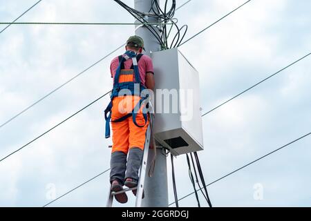 Perm, Russland - 25. August 2021: Elektriker oder Telekommunikationsleiter arbeitet an der Verlegung eines Kabels an der Spitze eines Telefonpols Stockfoto