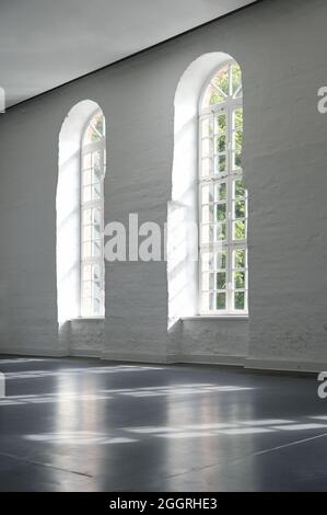 Zwei lange Bogenfenster in einer weiß gestrichenen Backsteinmauer im Innenbereich eines großen historischen Gebäudes, Architektur und Innenkonzept, Kopierraum, ausgewählt für Stockfoto