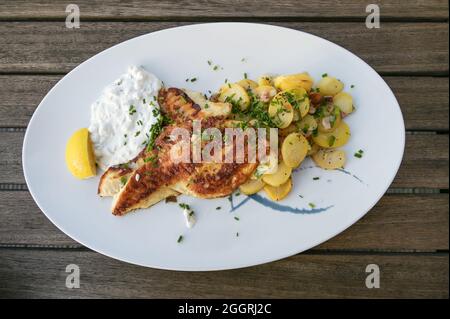 Saftig geröstetes Rotbarsch-Filet mit Bratkartoffeln und Remoulade-Dip auf einem Teller und auf einem rustikalen Holztisch, Blick von oben Stockfoto