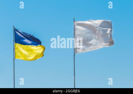 Nationalflagge der Ukraine, ein Symbol des Patriotismus und der Nation der Ukraine gegen den blauen Himmel gegenüber dem weißen Flaggenzeichen und Symbol der Güte und Stockfoto