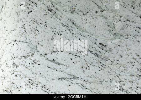 Die Textur aus weißem Stein mit Einschlüssen von schwarzen Punkten und Linien. Die Oberfläche des Felsens ist im Detail. Dekorativer Stein in natürlichem Licht. Stockfoto