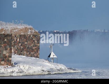 Mauern der Festungsinsel Suomenlinna an einem extrem kalten Wintertag mit Meeresnebel und eisiger Ostsee und Seespurschild (Leuchtturm) für m Stockfoto