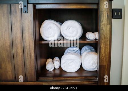 Aufgerollte weiße Handtücher, die in einem Schrank für die Gäste organisiert sind Stockfoto