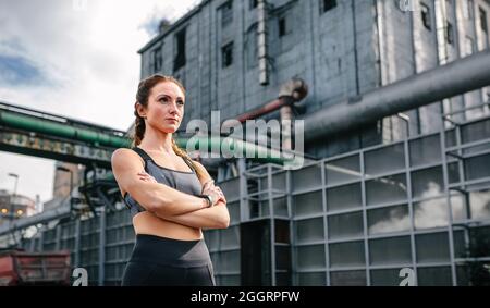 Sportlerin mit gekreuzten Armen vor einer Fabrik Stockfoto