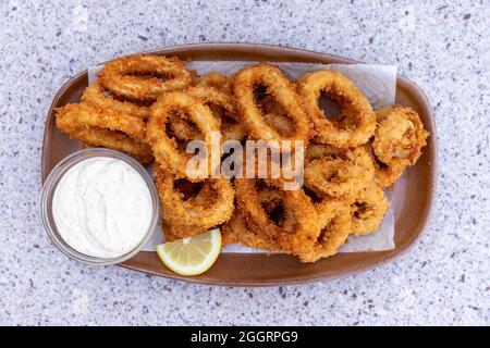 Draufsicht auf knusprig gebratene Calamari-Tintenringe mit Zitrone und Dipping-Sauce Stockfoto