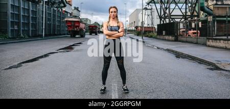 Eine Sportlerin aussehende Kamera, die vor einer Fabrik posiert Stockfoto