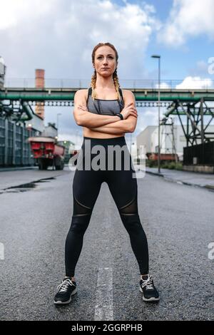 Sportlerin mit gekreuzten Armen vor einer Fabrik Stockfoto