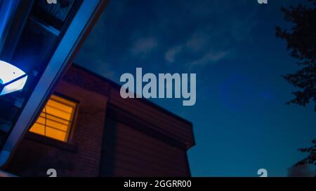 Orangefarbene Stadtlichter, Fenster, Straßen unter blauem und purpurfarbenem Sonnenuntergangshimmel mit Halbmond Stockfoto