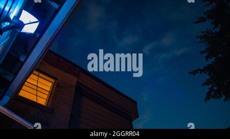 Orangefarbene Stadtlichter, Fenster, Straßen unter blauem und purpurfarbenem Sonnenuntergangshimmel mit Halbmond Stockfoto