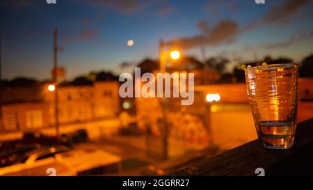 Orangefarbene Stadtlichter, Fenster, Straßen unter blauem und purpurfarbenem Sonnenuntergangshimmel mit Halbmond Stockfoto