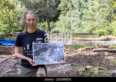 Natzwiller, Frankreich. August 2021. Die Grabungsleiterin Juliette Brangé steht auf den Grundmauern der ehemaligen Schmiede des Nazi-Konzentrationslagers Natzwiller-Struthof und hält ein historisches Foto des benachbarten Steinbruchs. Im ehemaligen Nazi-Konzentrationslager Natzwiller-Struthof führt ein Team der Universität Straßburg archäologische Ausgrabungen im Steinbruch und in der Lagerschmiede durch. Quelle: Philipp von Ditfurth/dpa/Alamy Live News Stockfoto