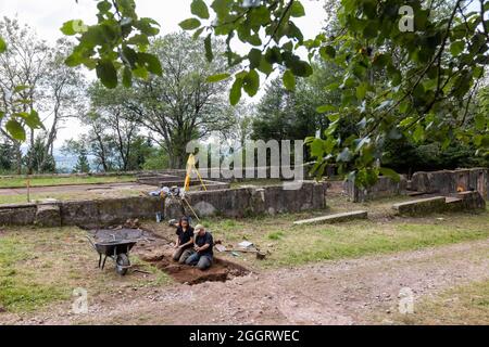 Natzwiller, Frankreich. August 2021. Zwei Mitarbeiter der Universität Straßburg graben mit Handinstrumenten nach Artefakten und Hinweisen, während die Grundmauern eines Gebäudes im Hintergrund zu sehen sind. Im ehemaligen Nazi-Konzentrationslager Natzwiller-Struthof führt ein Team der Universität Straßburg archäologische Ausgrabungen im Steinbruch und in der Lagerschmiede durch. Quelle: Philipp von Ditfurth/dpa/Alamy Live News Stockfoto