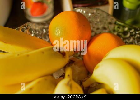 Orangen und Bananen in einer Glasvase auf dem Tisch. Frisches Obst zum Frühstück. Stockfoto