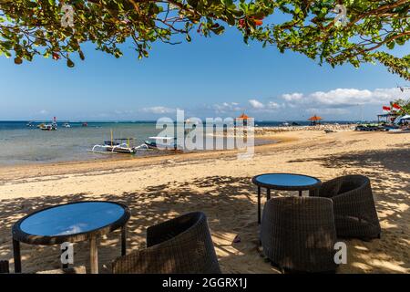 Blick auf Sanur Strand, Boote, Meer, Bäume. Cafe-Tische auf dem Sand. Bali, Indonesien. Stockfoto