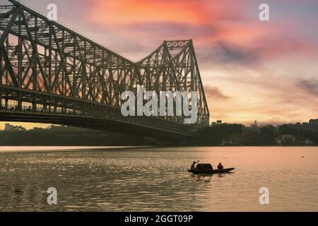 Howrah Brücke bei Sonnenuntergang mit Blick auf ein Fischerboot auf dem Fluss Ganges und Kalkutta Stadtbild Stockfoto