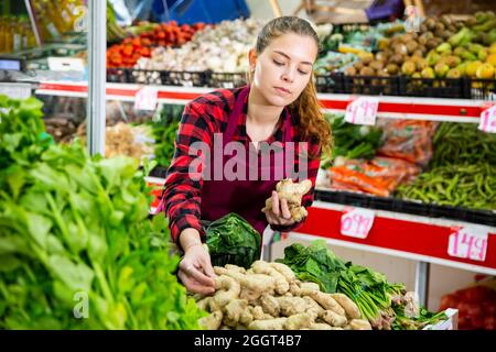 Lächelnde Verkäuferin legte Ingwer auf die Theke Stockfoto