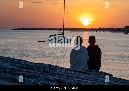 Junges Paar, das den Sonnenaufgang über Matanzas Bay und Anastasia Island von der Küste von Castillo de San Marcos in St. Augustine, Florida, aus beobachtet. (USA) Stockfoto