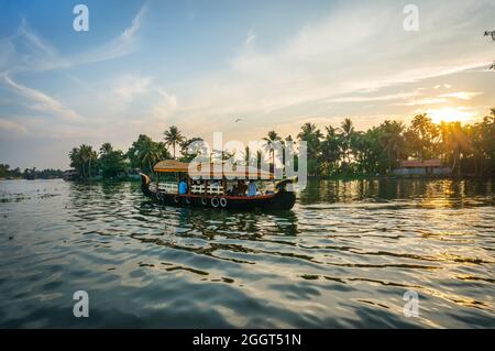 Boot mit Touristen, die auf einem Hintergrund aus Palmen und einem wunderschönen Sonnenuntergang den Fluss hinunter schweben. Die Sonne untergeht über dem Horizont und Shine through the Stockfoto