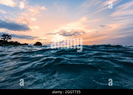 (Selektiver Fokus) atemberaubende Aussicht auf ein raues Meer mit einigen Wellen im Vordergrund und einem dramatischen Sonnenaufgang in der Ferne. Sardinien, Italien. Stockfoto