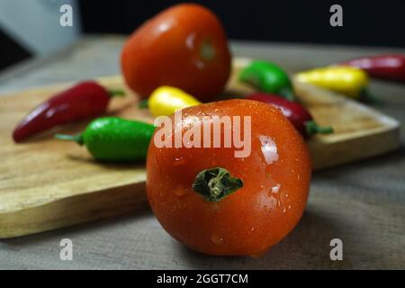 Nahaufnahme von reifen Tomaten und Paprika mit Wassertropfen auf einer Holzoberfläche Stockfoto
