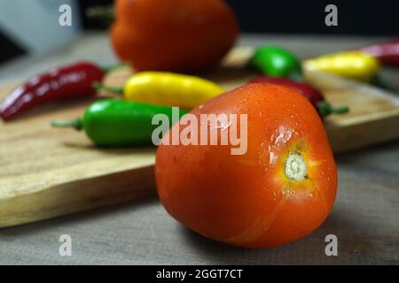 Nahaufnahme einer reifen Tomate und scharfer Paprika mit Wassertropfen auf einer Holzoberfläche Stockfoto