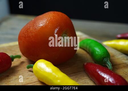 Nahaufnahme einer reifen Tomate und scharfer Paprika mit Wassertropfen auf einer Holzoberfläche Stockfoto