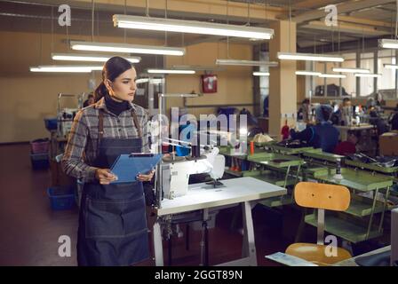 Ernsthafter Arbeiter, der in einer großen Nähwerkstatt in der Schuhfabrik steht Stockfoto