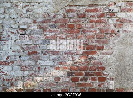 Vorderansicht einer alten, schmutzigen, beschädigten und verputzten Wand. Der Putz wird meist abgeschält und zeigt alte Ziegelsteine. Strukturierter Hintergrund im Vollformat. Stockfoto