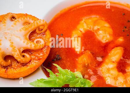 Schüssel Tomatensuppe mit Garnelen mit einem kleinen Oktopus auf einer Orangenscheibe gebacken. Nahaufnahme, Draufsicht Stockfoto