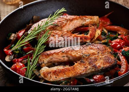 Gusseiserne Pfanne gekocht Alaska Wildlachs mit Kirschtomaten, Pfeffer, Pilze, Zwiebeln und Kräutern Stockfoto