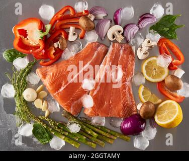 Frische rohe Lachsfilets mit Gemüse auf Eis auf einem Schneidebrett aus Edelstahl Stockfoto