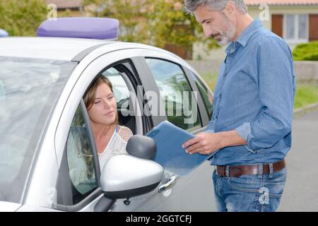 Die Fahrschullehrerin stand vor dem Auto und sprach mit der Lernerin Stockfoto